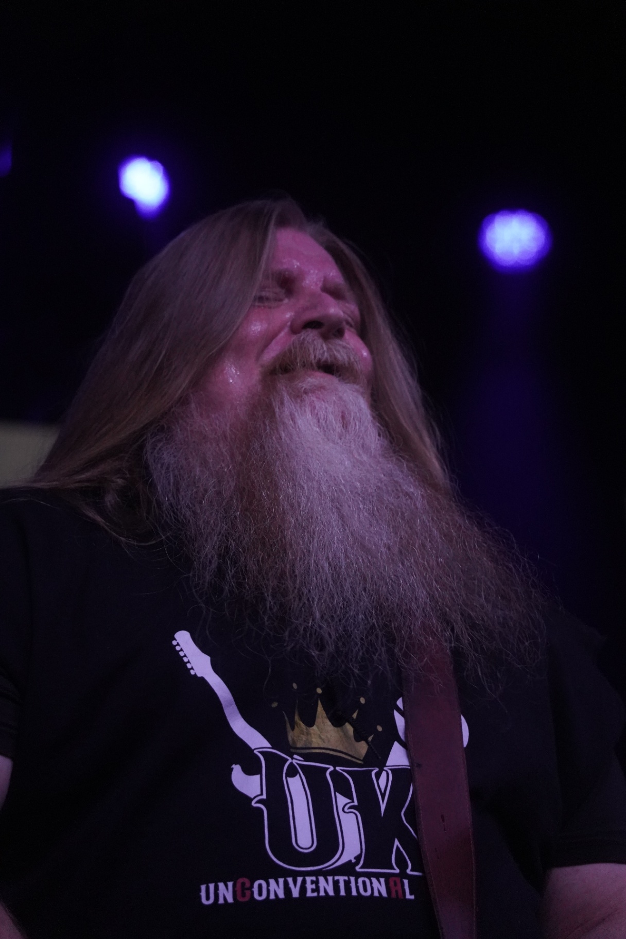 Long-bearded guitarist looking up into purple stage lights