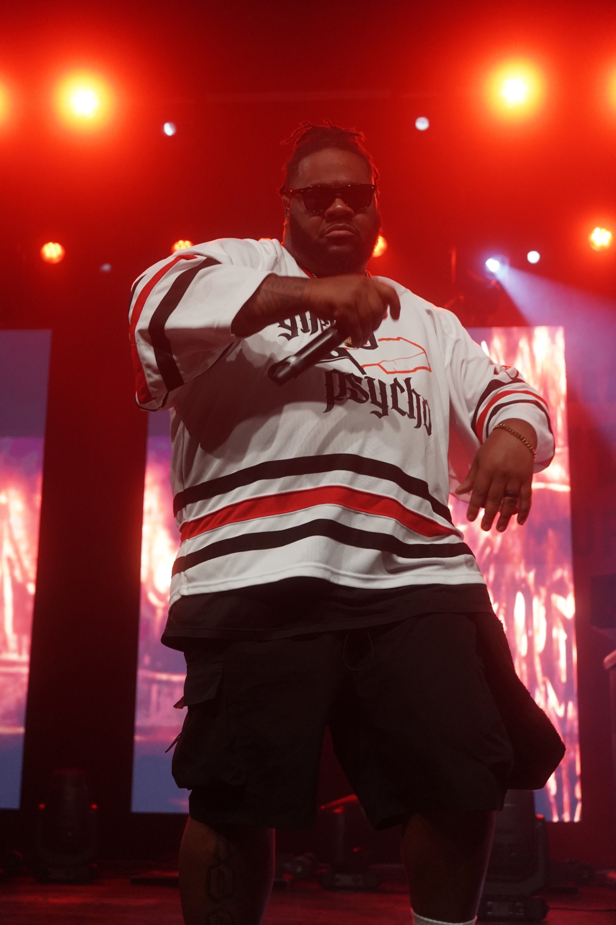 Rapper in Ghetto Psycho hockey jersey pointing mic at crowd under red lights