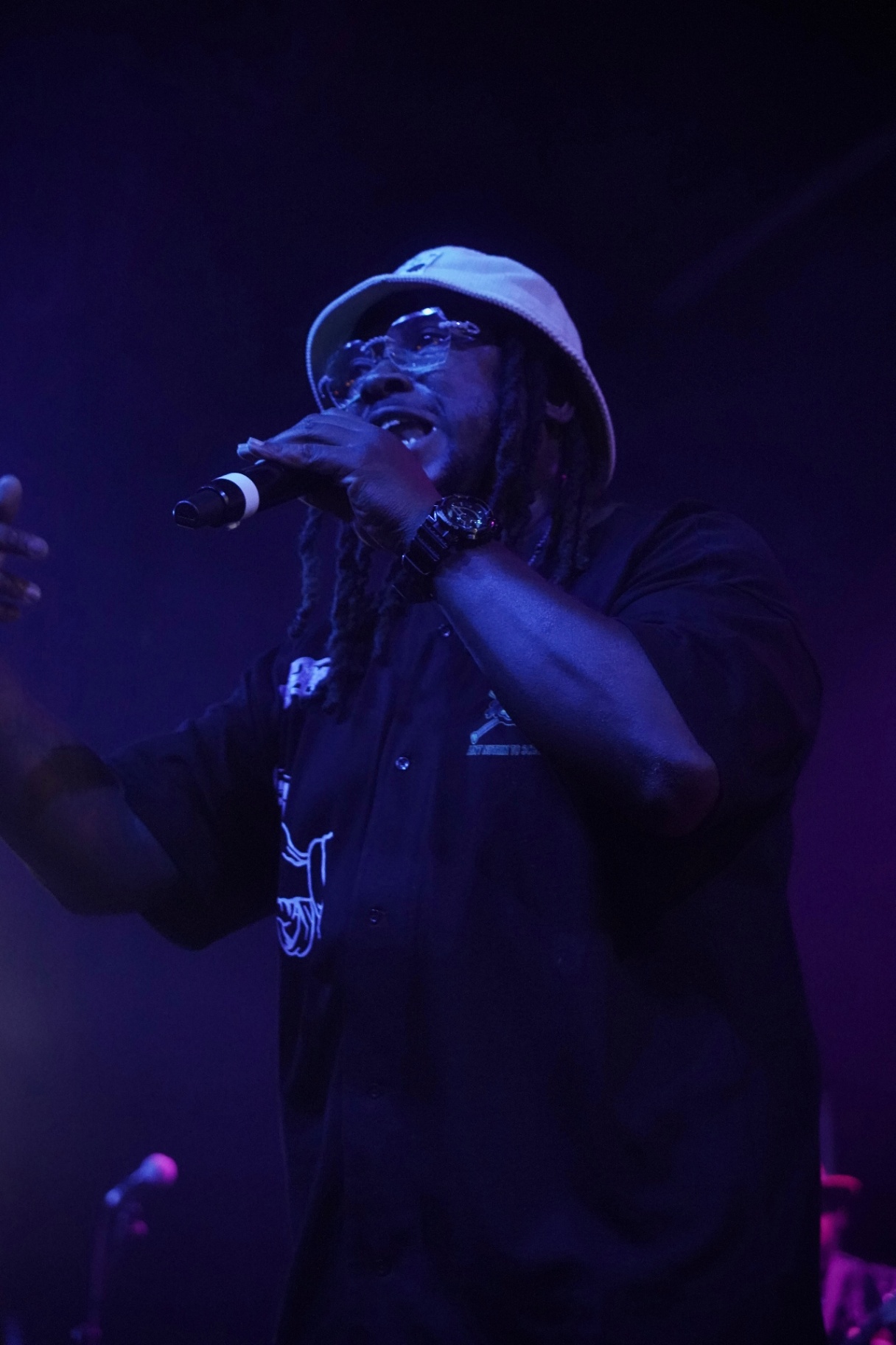 Rapper in bucket hat gripping the mic under blue and purple stage light