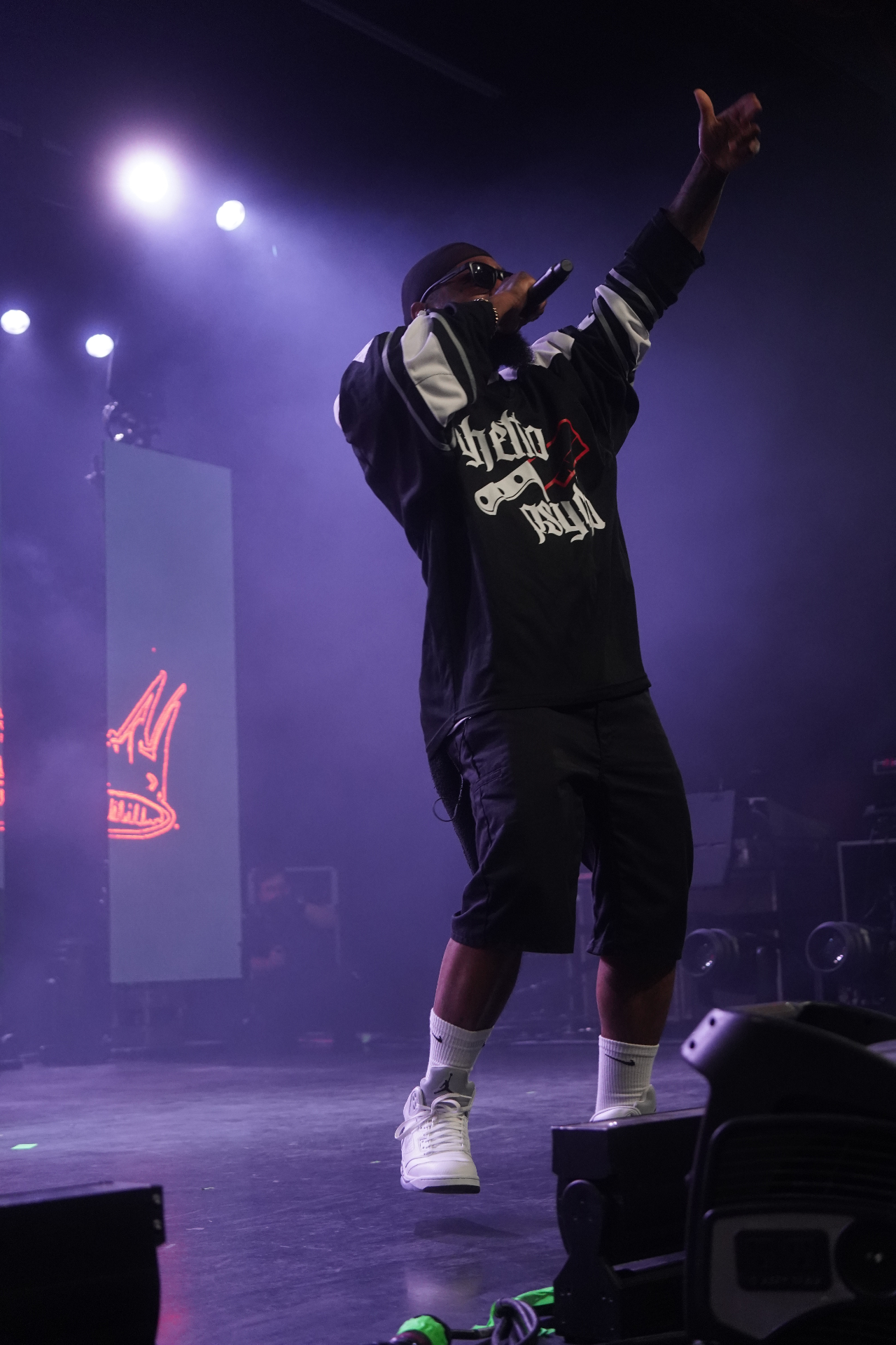 Rapper mid-jump with arm raised under purple lights