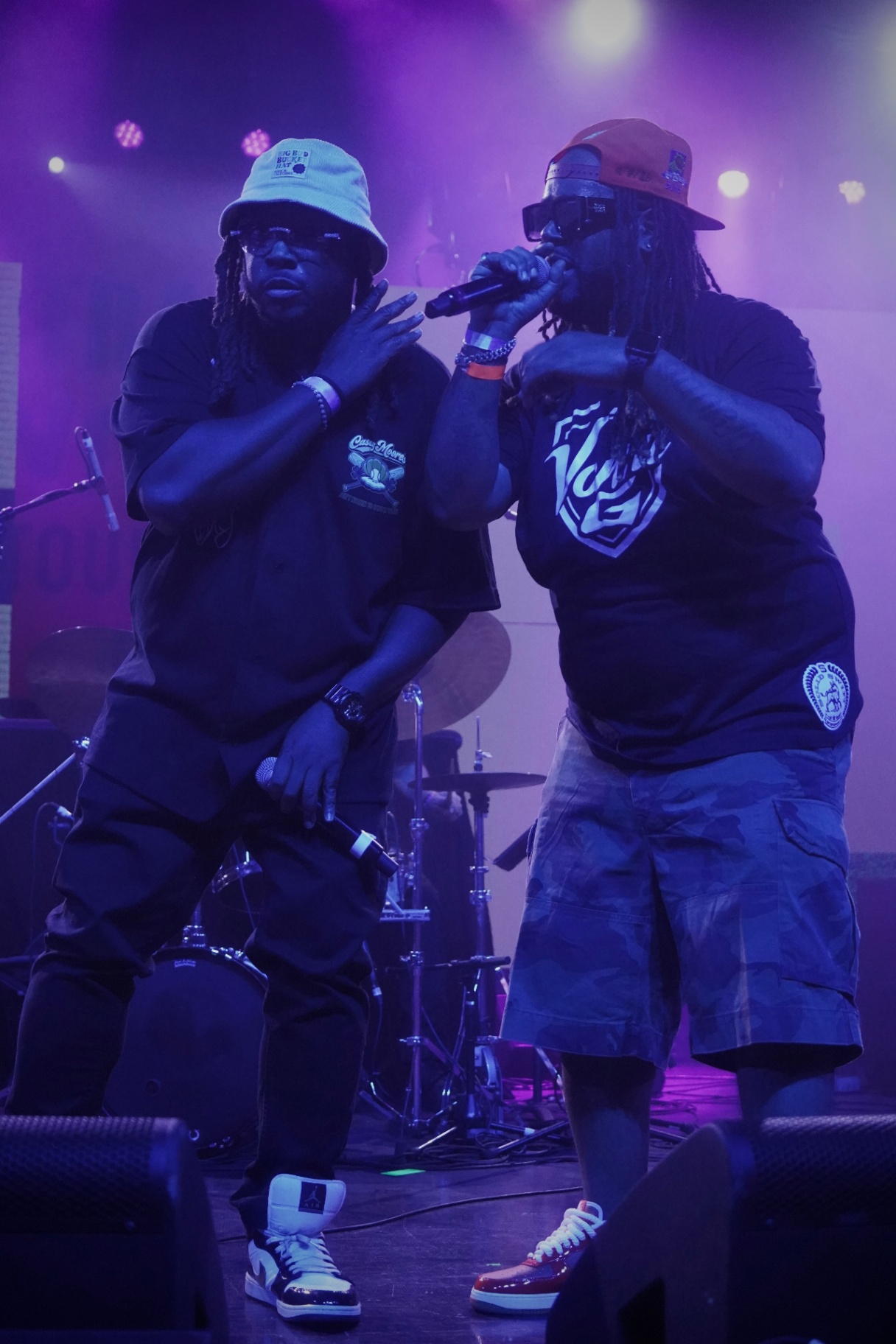 Two rappers on stage together bathed in purple light