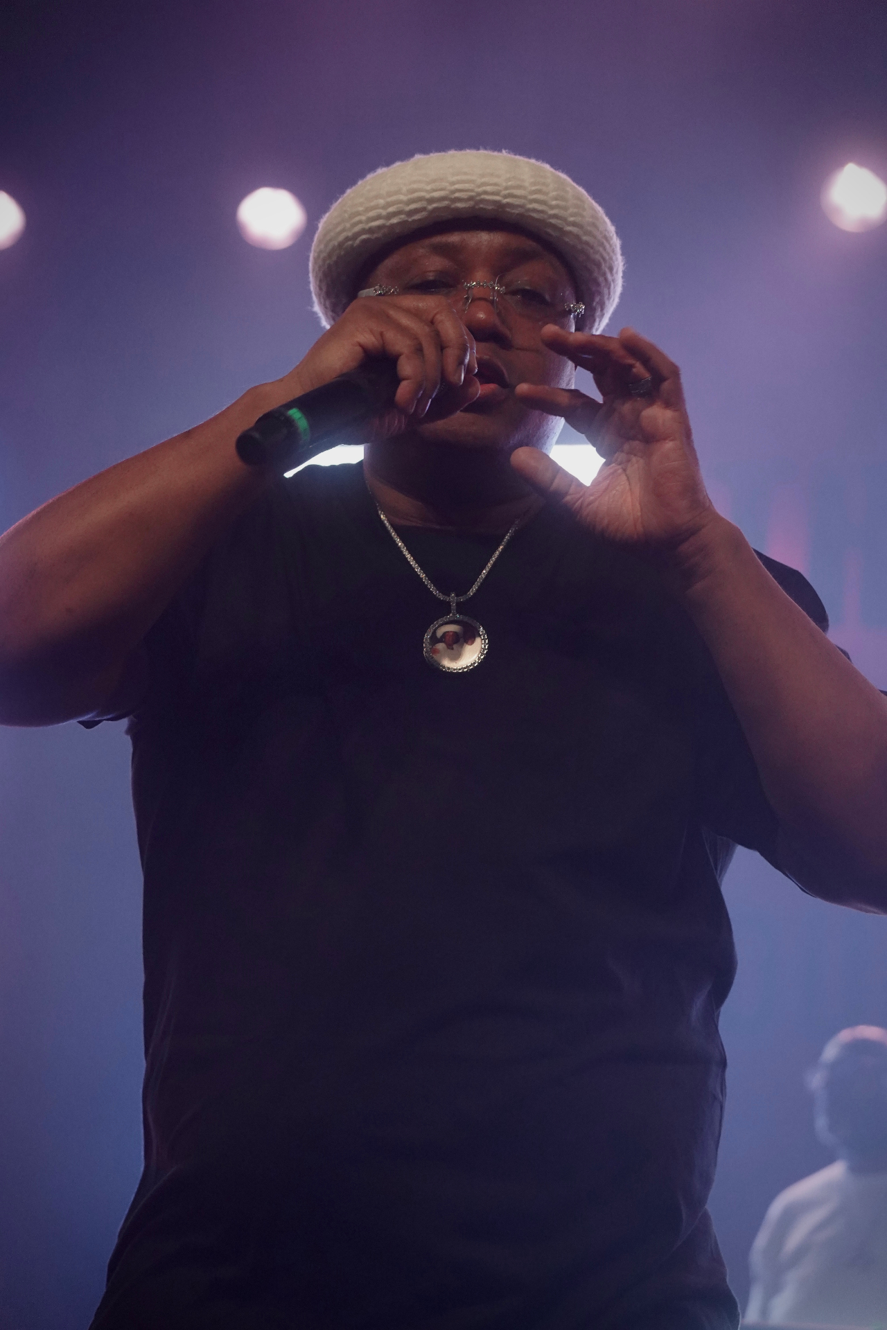 E-40 gesturing with mic in white bucket hat under purple light