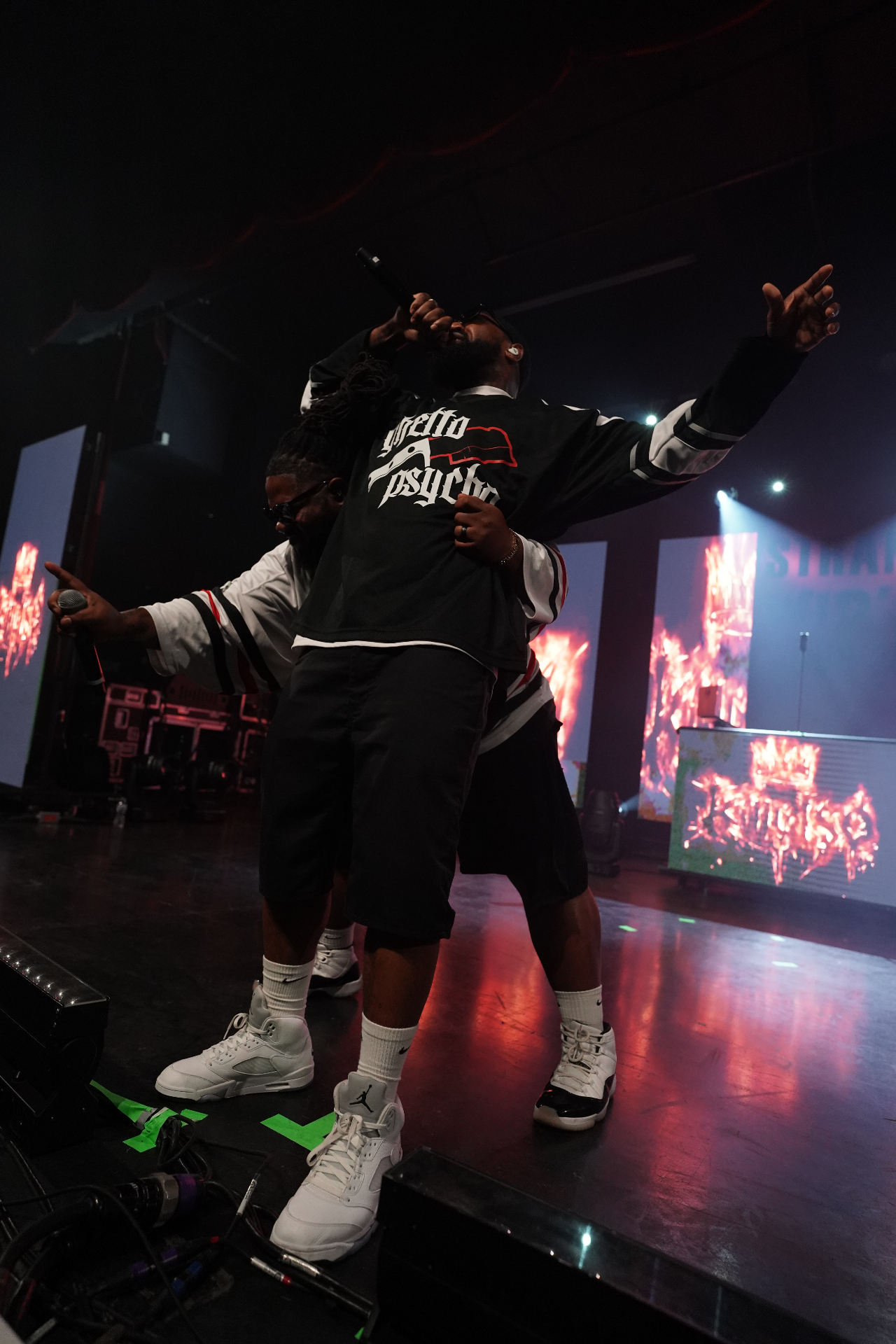 Two performers embracing on stage with fiery visuals