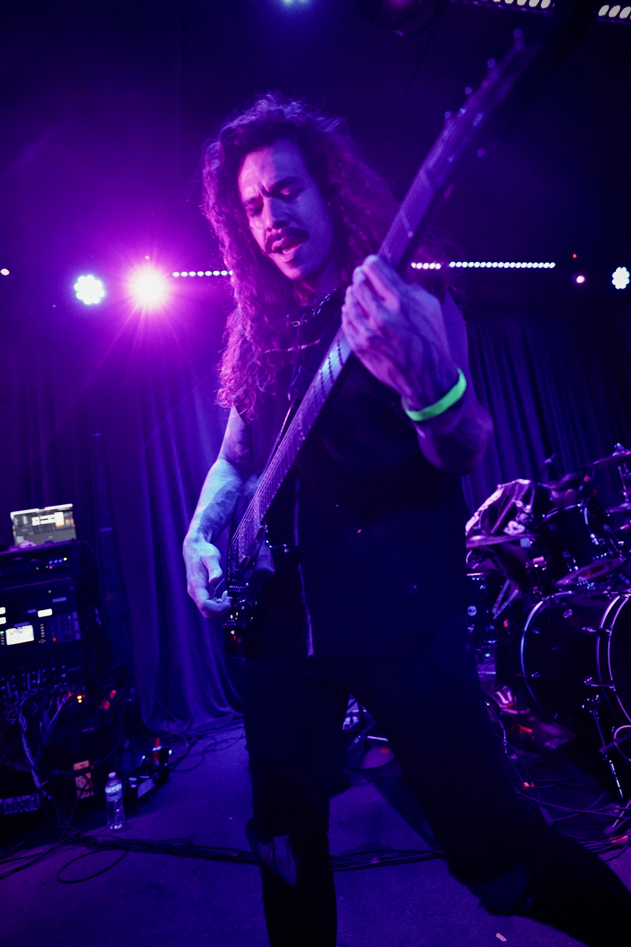 Long-haired bassist under purple stage lights
