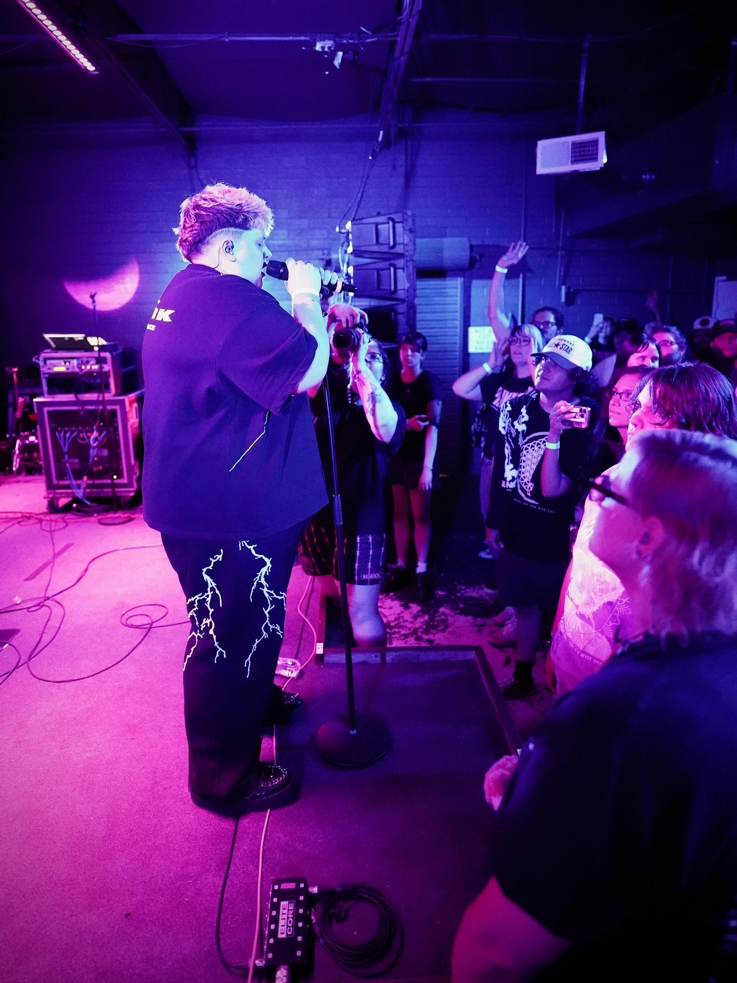 Vocalist facing the crowd in lightning-print pants under purple light