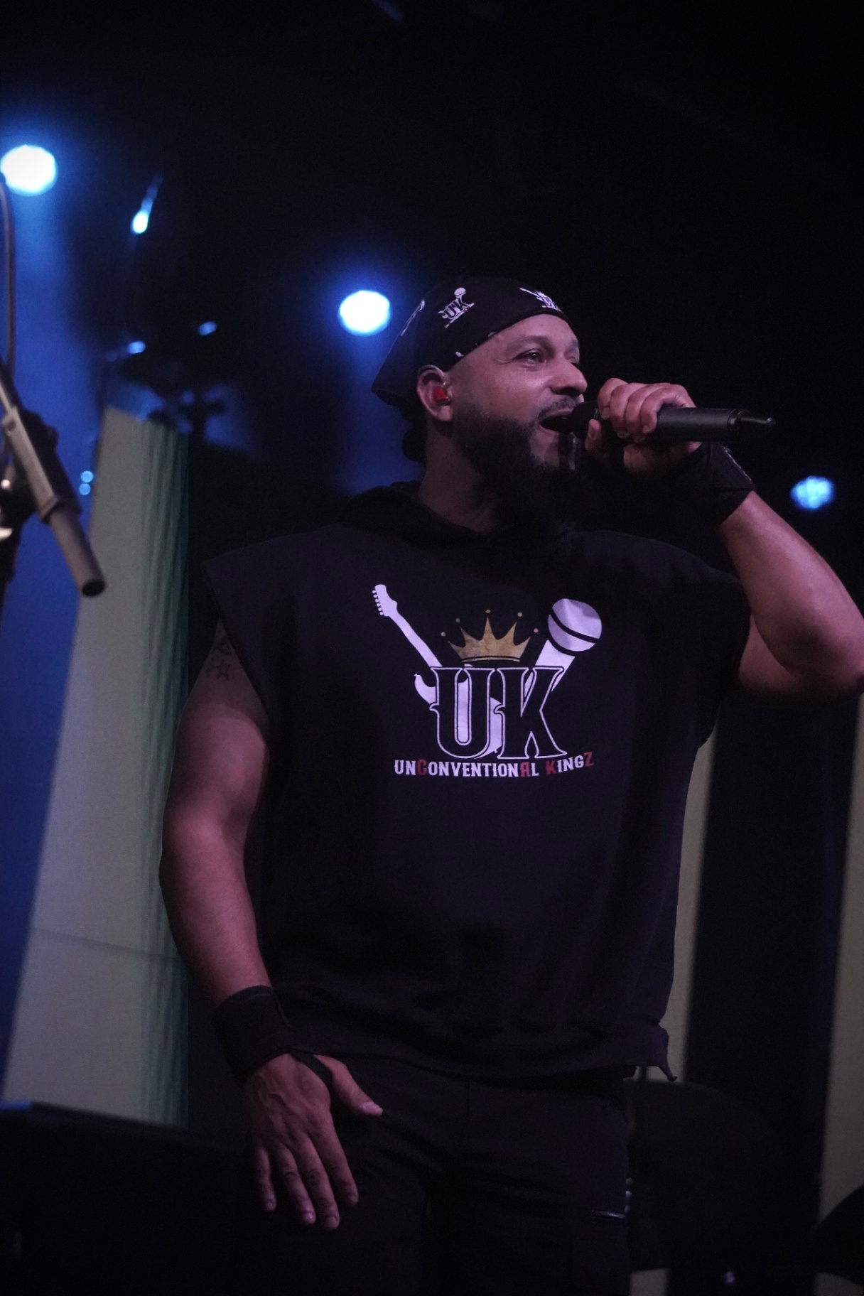 Rapper in UK sleeveless hoodie on the mic under blue light