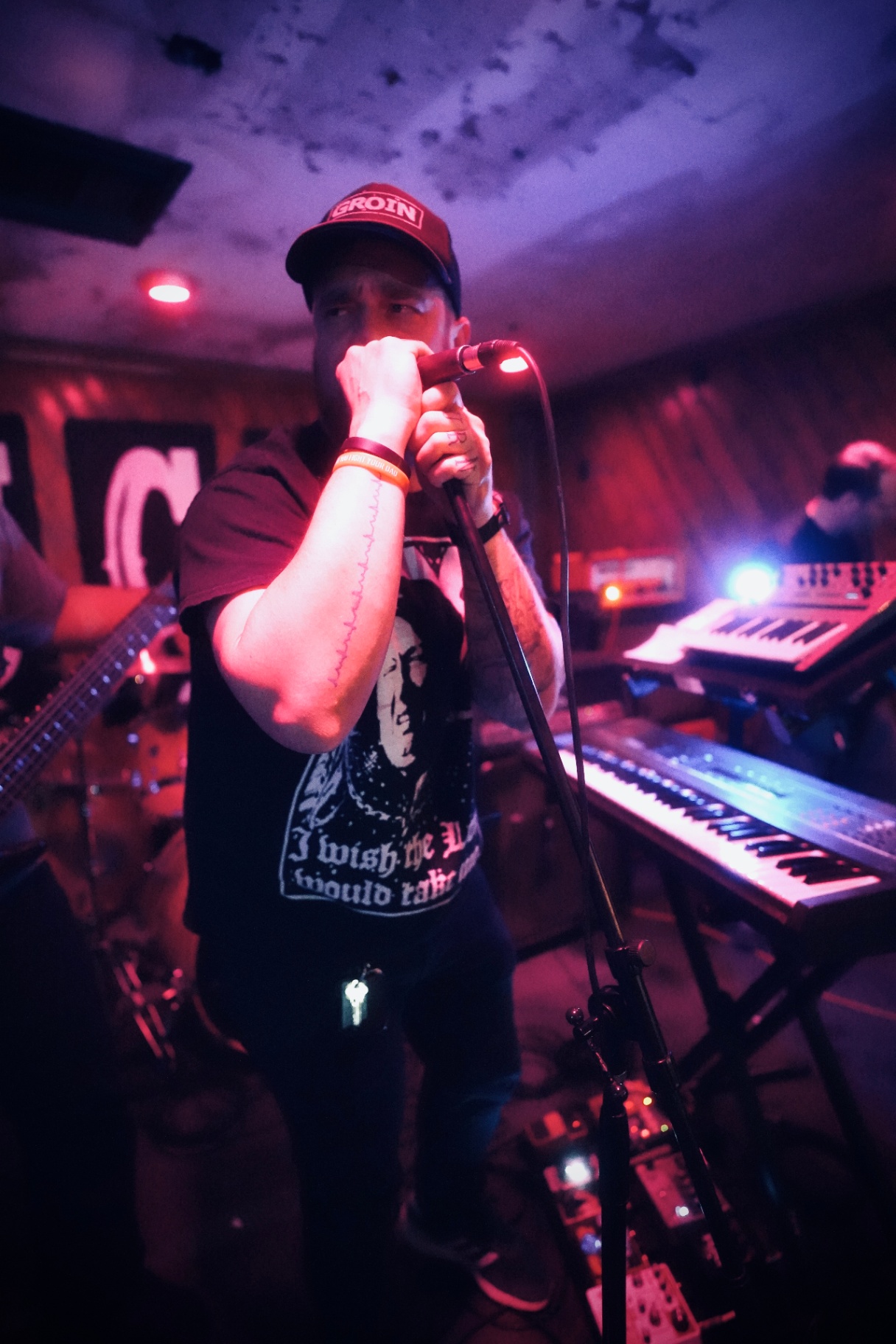 Vocalist gripping the mic with keyboards behind him in red light