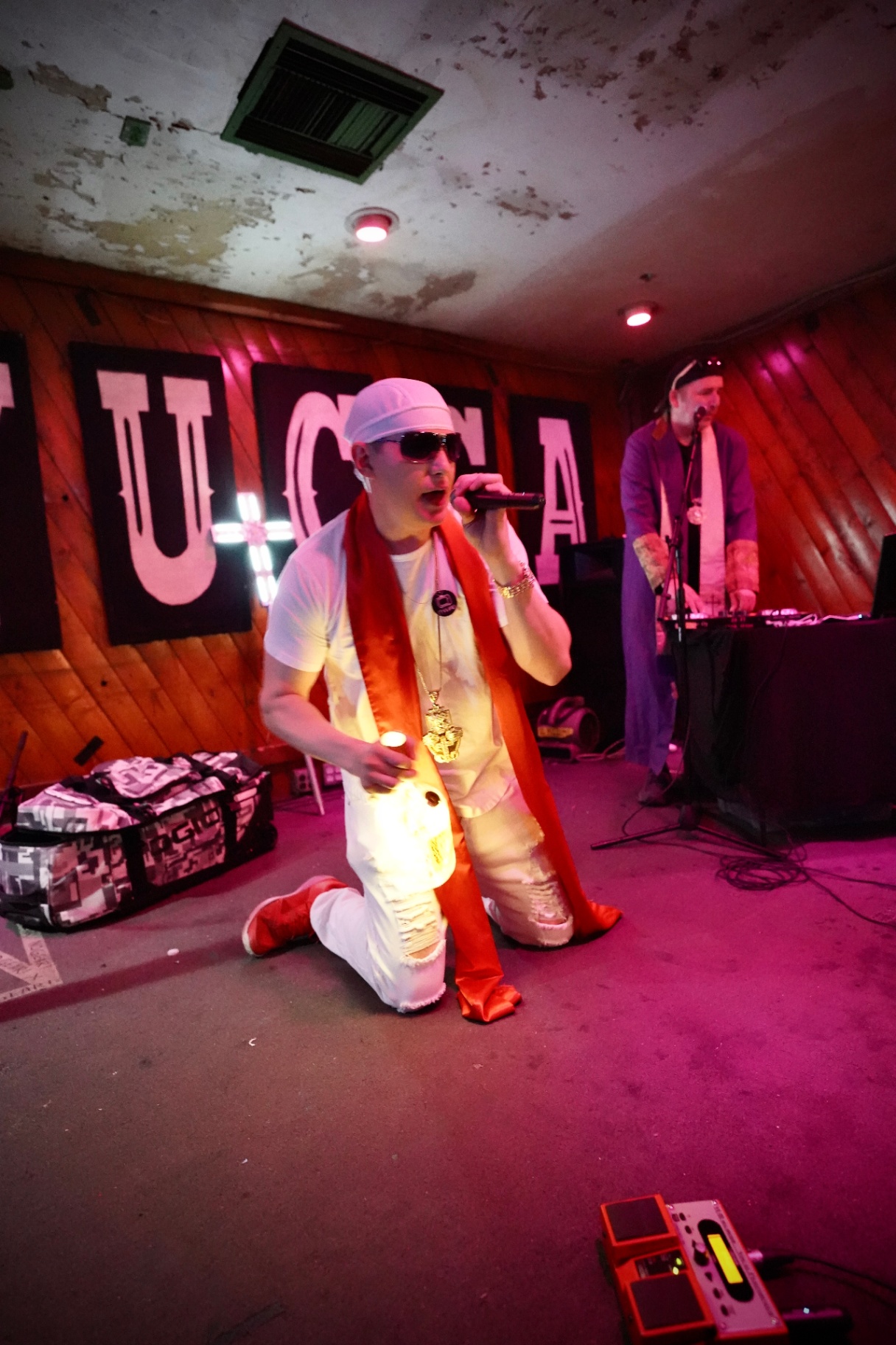Rapper on his knees performing with DJ in the background