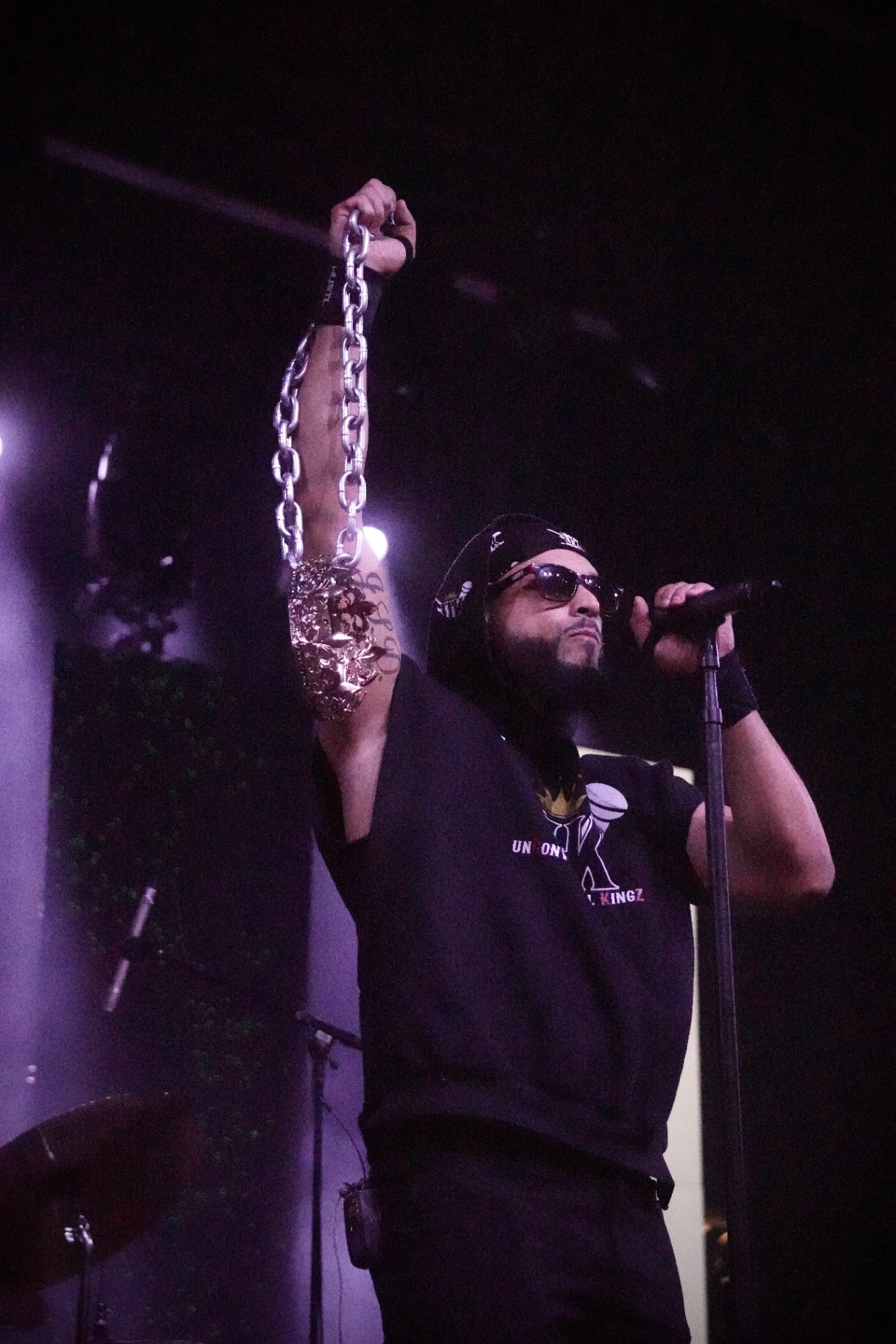 Rapper holding a heavy silver chain overhead with mic in hand