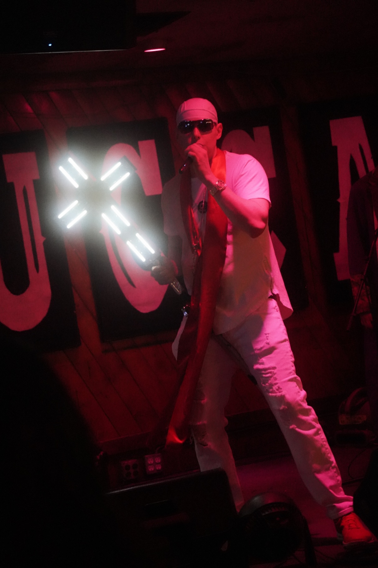 Rapper in white with red scarf holding an illuminated X prop