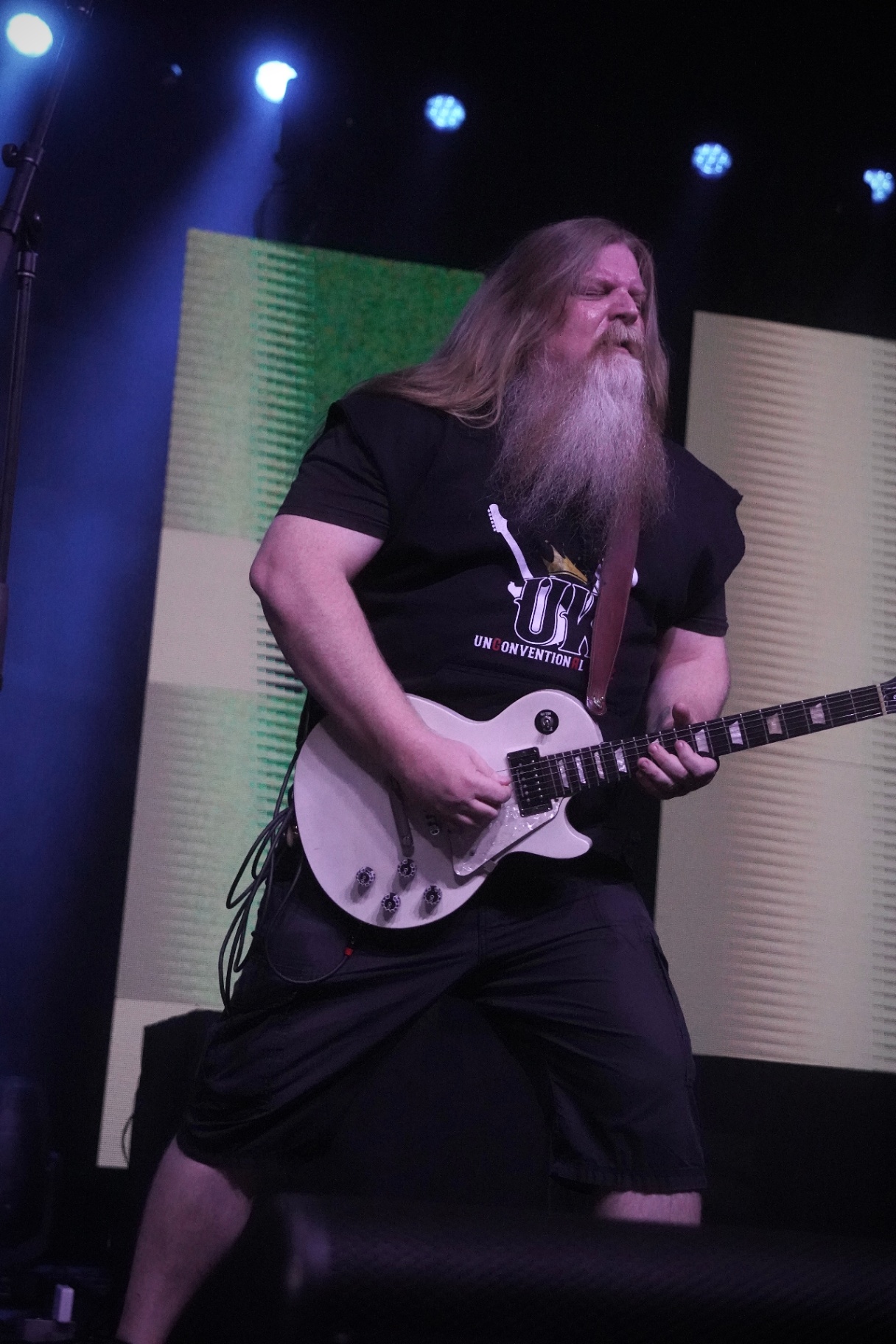 Bearded guitarist shredding a white Les Paul under blue lights
